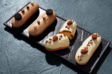 Board with delicious eclairs on dark background