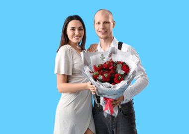 Young couple with bouquet of flowers on blue background. Valentine's Day celebration