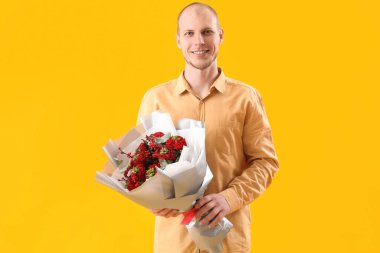 Young man with bouquet of flowers on yellow background. Valentine's Day celebration