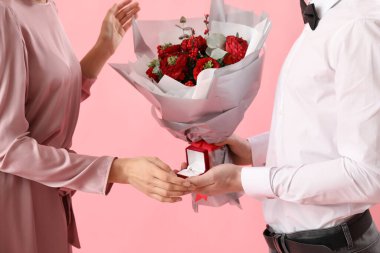 Young man with flowers and ring proposing to his girlfriend on pink background, closeup. Valentine's Day celebration