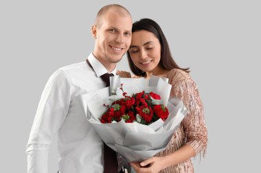 Young couple with bouquet of flowers on light background. Valentine's Day celebration