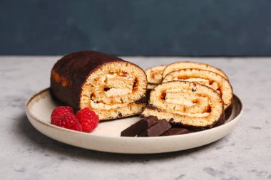 Plate with pieces of tasty sponge cake roll, chocolate and raspberry on grunge background