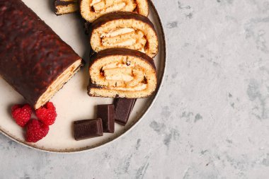 Plate with pieces of tasty sponge cake roll, chocolate and raspberry on grunge background, closeup