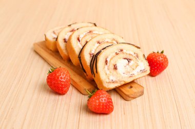 Cutting board with tasty pieces of sponge cake roll and strawberry on wooden background