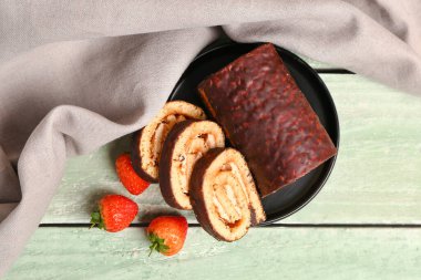 Plate with tasty sponge cake roll and strawberry on green wooden background