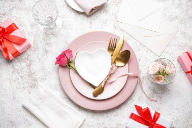 Table setting for Valentine's Day with roses and gift on light grunge background
