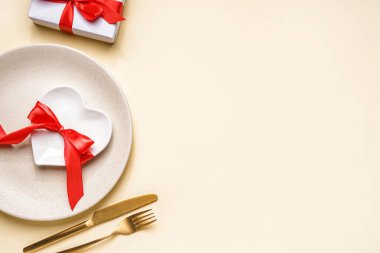 Table setting for Valentine's Day with gift on beige background
