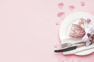Table setting for Valentine's Day with glass and hearts on pink background