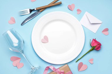 Table setting for Valentine's Day with rose and hearts on blue background