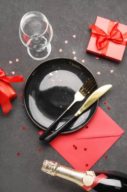 Table setting for Valentine's Day with bottle of champagne and envelope on black table