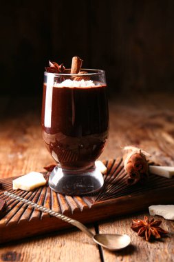 Board with glass of delicious chocolate pudding, anise, cinnamon and coconut shavings on wooden background