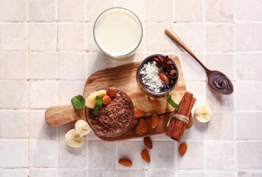 Board with glasses of delicious chocolate pudding, cinnamon, almond and milk on tile table