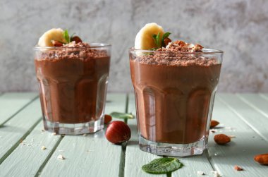 Glasses of delicious chocolate pudding with almond, banana and mint on green wooden table