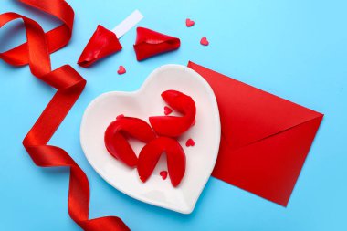 Plate of fortune cookies with envelope and ribbon on blue background. Valentine's Day celebration