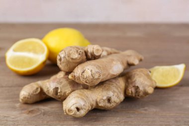 Fresh ginger roots and lemon pieces on wooden table