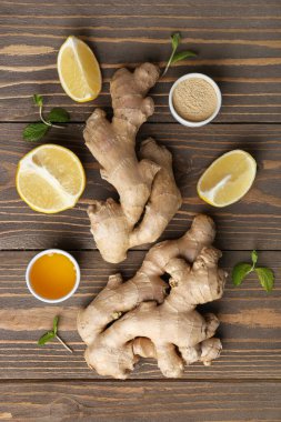 Composition with ginger roots, lemon pieces and bowl of honey on wooden background