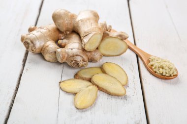 Fresh ginger, slices and spoon on wooden background