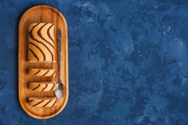 Board with pieces of delicious sponge cake roll on blue table
