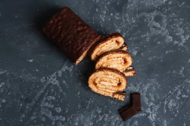 Pieces of delicious sponge cake roll and chocolate on grey table