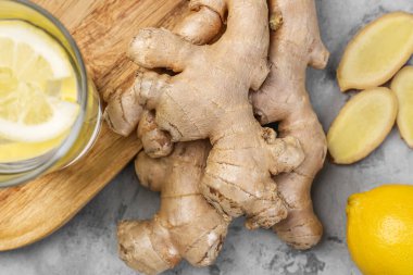 Cutting board with fresh ginger roots, lemon and glass of water on grunge background, closeup