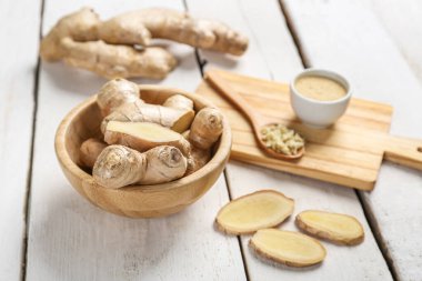 Wooden plate with ginger roots, cutting board and powder on light wooden background