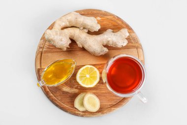 Board with ginger roots, cup of black tea, honey and lemon on grey background