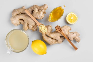 Ginger roots, cup of tea, lemon and honey on grey background