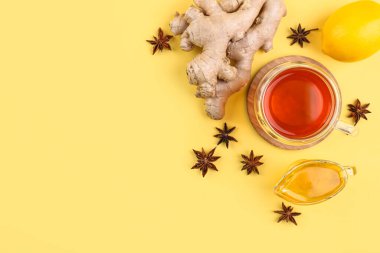 Ginger roots, cup of black tea, lemon, honey and anise on yellow background