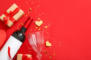 Composition with bottle of wine, glass and gifts on red background. Valentines Day celebration