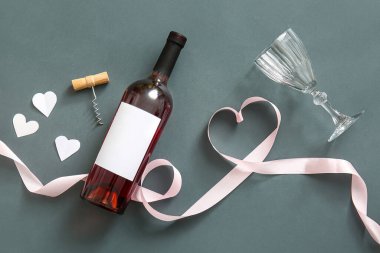 Composition with bottle of wine, glass, corkscrew and ribbon on dark background. Valentines Day celebration