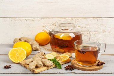 Ginger root, glass cup of black tea, teapot, and lemon on wooden table