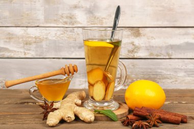 Glass of tea with sliced ginger root, lemon and cinnamon on wooden background