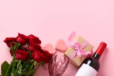 Bottle of wine, rose flowers, gift and heart-shaped cookies on pink background. Valentine's Day celebration