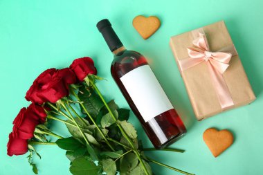 Bottle of wine, rose flowers, heart-shaped cookie and gift on turquoise background. Valentine's Day celebration