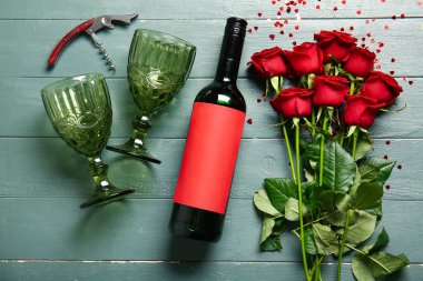 Bottle of wine, rose flowers and glasses on green wooden background. Valentine's Day celebration