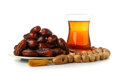 Plate with dried dates, prayer beads and glass of tea for Ramadan on white background