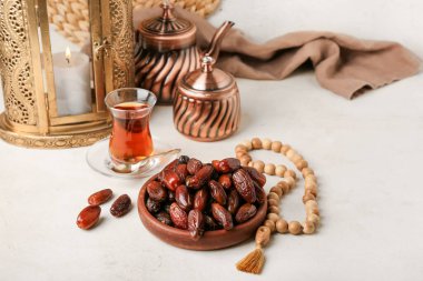 Bowl with dates, glass of tea and prayer beads for Ramadan on light table