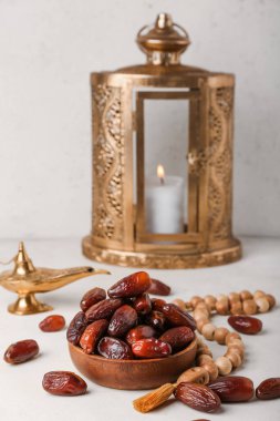 Bowl with dates, prayer beads, Muslim lamp and lantern for Ramadan on light background