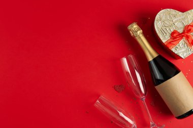 Bottle of wine, heart-shaped gift and glasses on red background. Valentine's Day Celebration