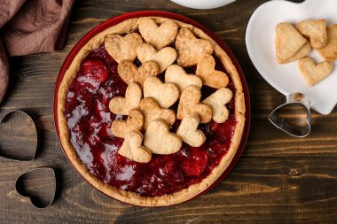 Plate with sweet strawberry pie and heart-shaped plate of cookie hearts for Valentine's day on wooden background