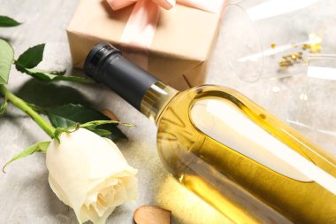 Bottle of wine, gift box, rose flower and glasses on grey table. Valentine's Day celebration