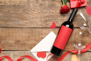 Bottle of wine, envelope, glasses and rose flower on wooden background. Valentine's Day celebration