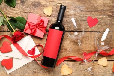 Bottle of wine, rose flower, envelope and gift box on wooden background. Valentine's Day celebration