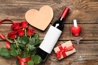 Bottle of wine, decorative hearts, gift box and rose flowers on wooden background. Valentine's Day celebration