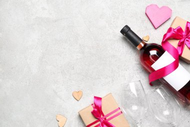 Bottle of wine, gift boxes, paper hearts and glasses on grey table. Valentine's Day celebration