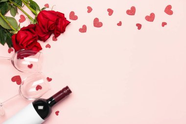 Frame made of wine bottle, glasses, hearts and rose flowers on pink background. Valentine's Day celebration
