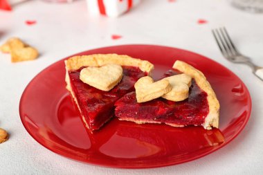 Red plate with pieces of sweet strawberry pie and cookie hearts for Valentine's day on white table