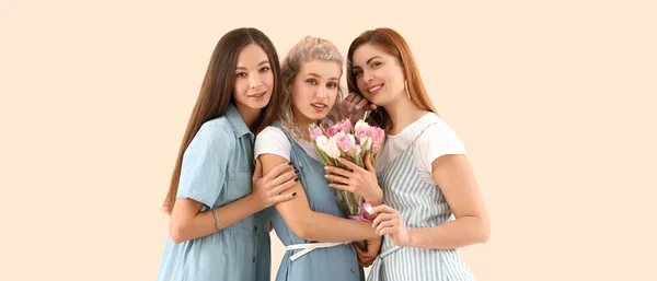 Beautiful young women with tulips on beige background. International Women\'s Day celebration