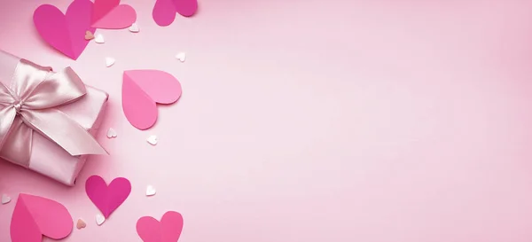 Gift with paper hearts and sprinkles on pink background with space for text. Valentines Day celebration