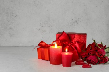 Burning candles, beautiful rose flowers and gift boxes on light background. Valentine's Day celebration